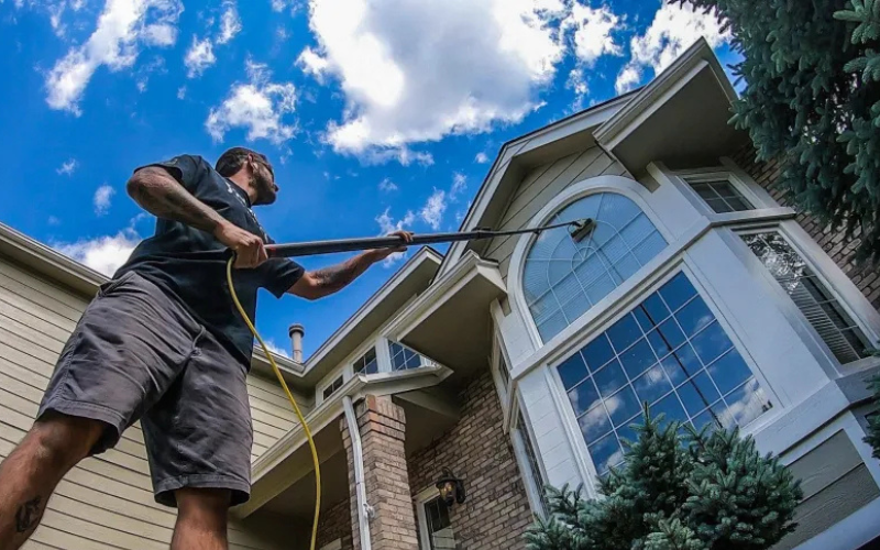 Man holding a long pole that is spraying cleaner for window washing