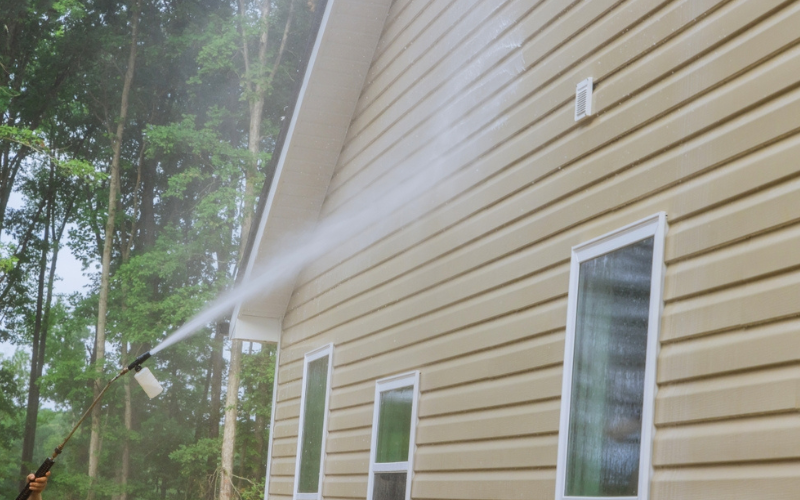 Man holding a long pole that is spraying cleaner for window washing